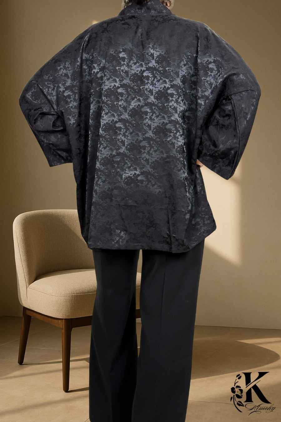 Kimono noir à motifs délicats porté avec un pantalon noir, sur fond clair et texturé
