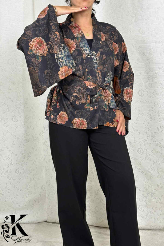 Femme portant un kimono noir à motifs floraux colorés, posant dans un décor sobre avec une lumière douce