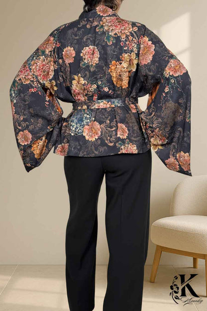Kimono femme chic à fleurs roses sur fond noir, ceinturé, porté avec un pantalon noir dans un décor sobre