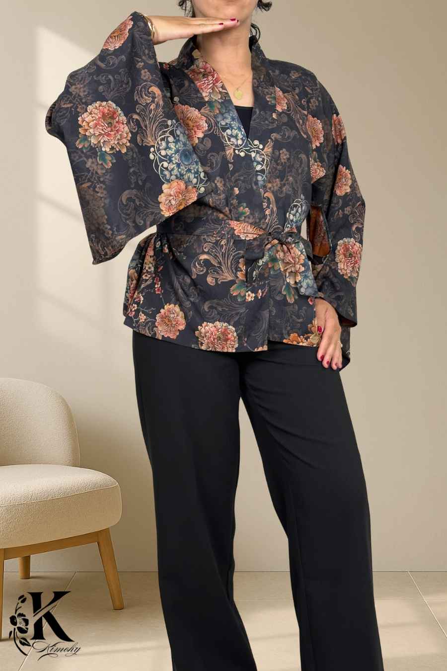 Femme portant un kimono noir à motifs floraux colorés, posant dans un décor sobre avec une lumière douce