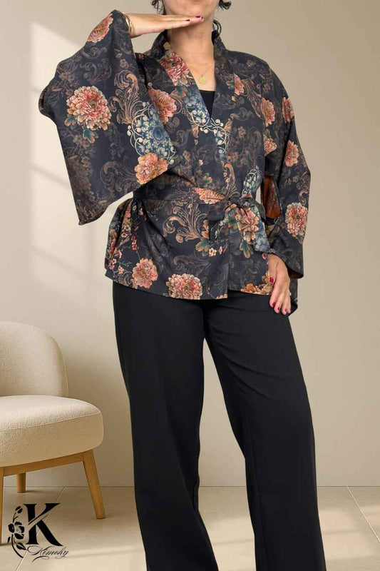 Femme portant un kimono noir à motifs floraux colorés, posant dans un décor sobre avec une lumière douce