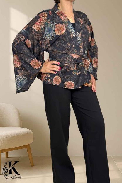 Femme portant un kimono noir à motifs floraux, avec des manches larges, dans un décor sobre et élégant