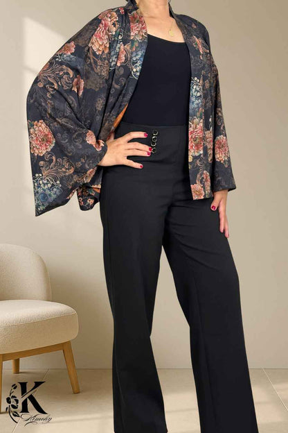 Femme portant un kimono à motifs floraux sur fond noir, avec un pantalon noir élégant, dans un décor sobre