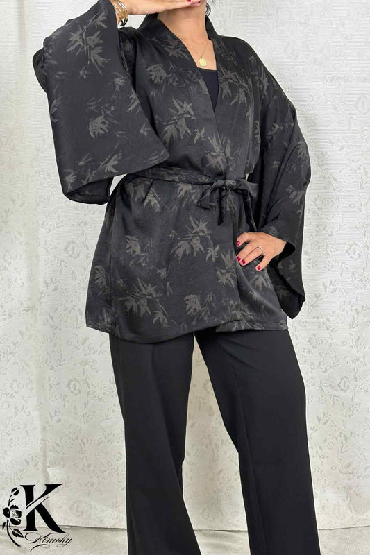 Femme en kimono noir à motifs de feuilles, posant dans un décor clair avec des motifs subtils