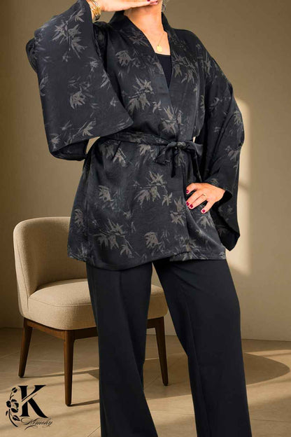 Femme en kimono noir à motifs de feuilles, posant dans un décor clair avec des motifs subtils
