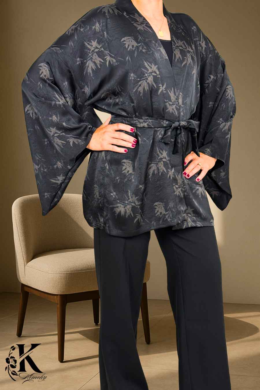 Femme en kimono noir à motifs de feuilles, posant dans un décor clair avec des pantalons noirs