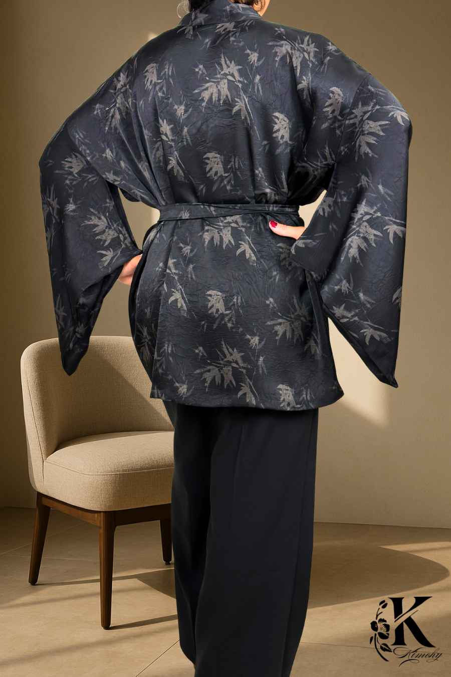 Femme portant un kimono noir avec motifs de bambous, dans un décor clair et texturé, avec des manches larges