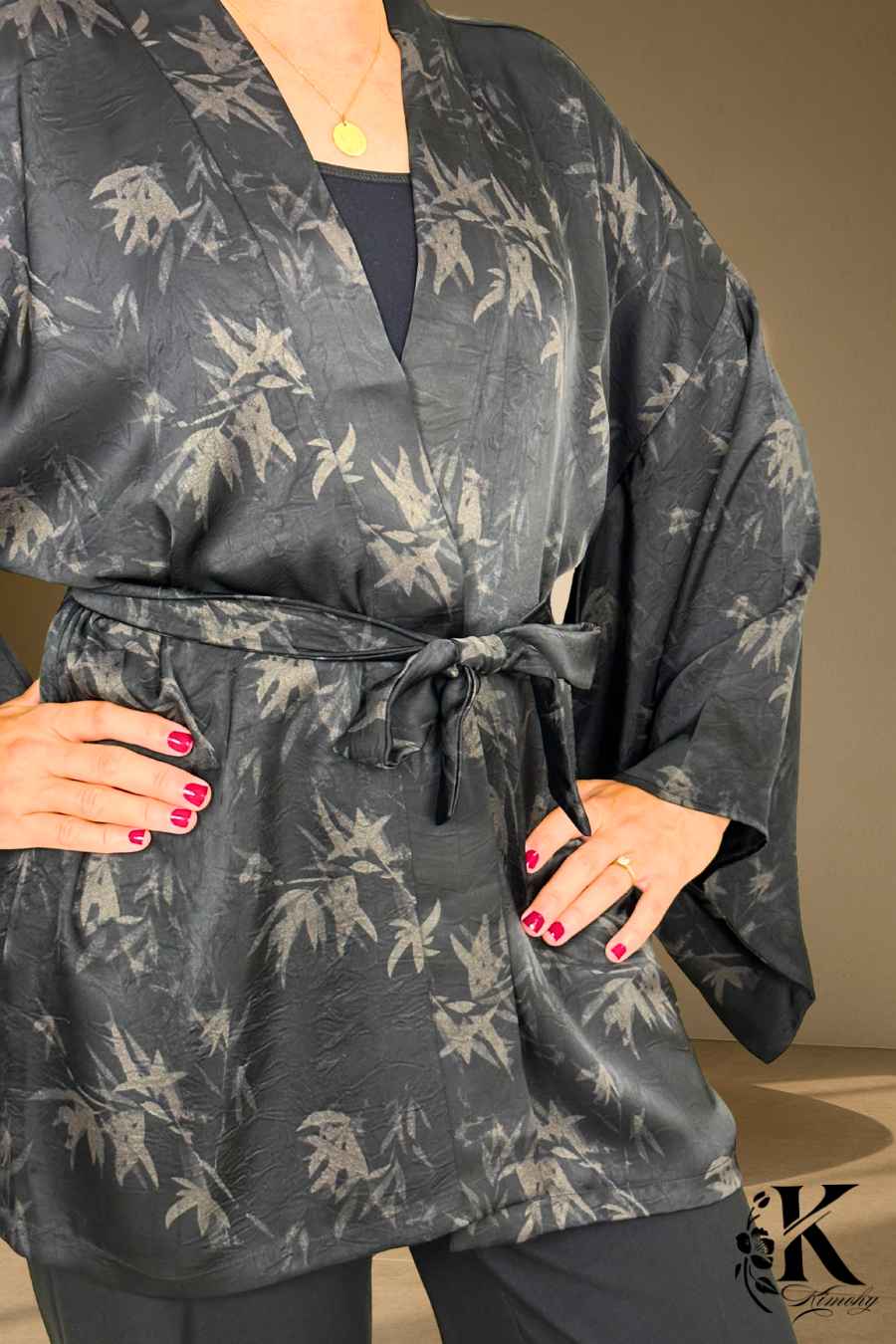 Kimono noir avec motifs de feuilles grises, ceinturé, porté par une femme dans un décor sobre