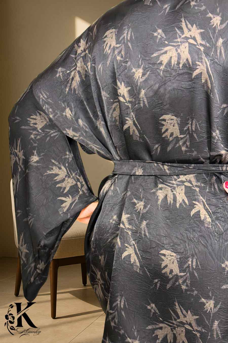 Kimono noir à motifs de feuilles grises, avec une ceinture, porté dans un décor sobre et élégant