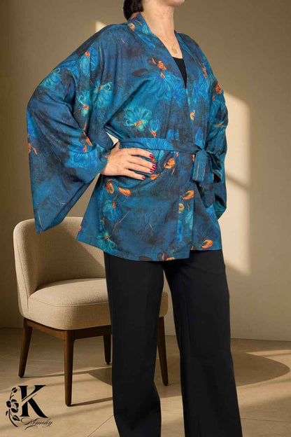 Femme en kimono bleu avec motifs floraux, posant dans un décor clair et texturé, ceinture nouée à la taille