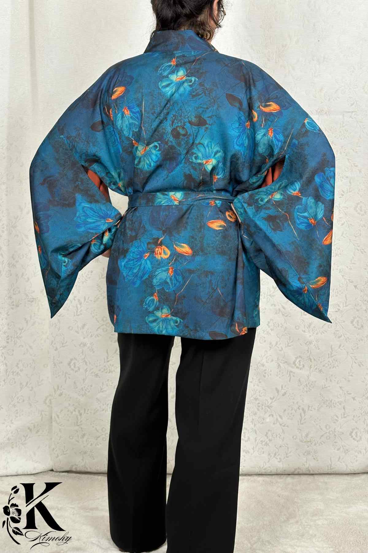 Kimono femme chic en tissu bleu avec motifs floraux, porté avec un pantalon noir dans un décor sobre