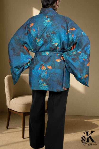 Kimono femme chic en tissu bleu avec motifs floraux, porté avec un pantalon noir dans un décor sobre