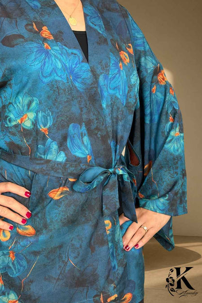 Kimono en tissu bleu avec motifs floraux orange, porté par une femme dans un décor sobre et élégant