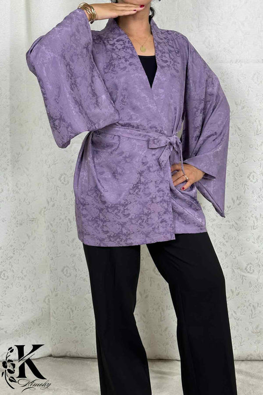 Veste kimono femme en tissu violet avec motifs subtils, portée avec un pantalon noir et un décor floral en arrière-plan