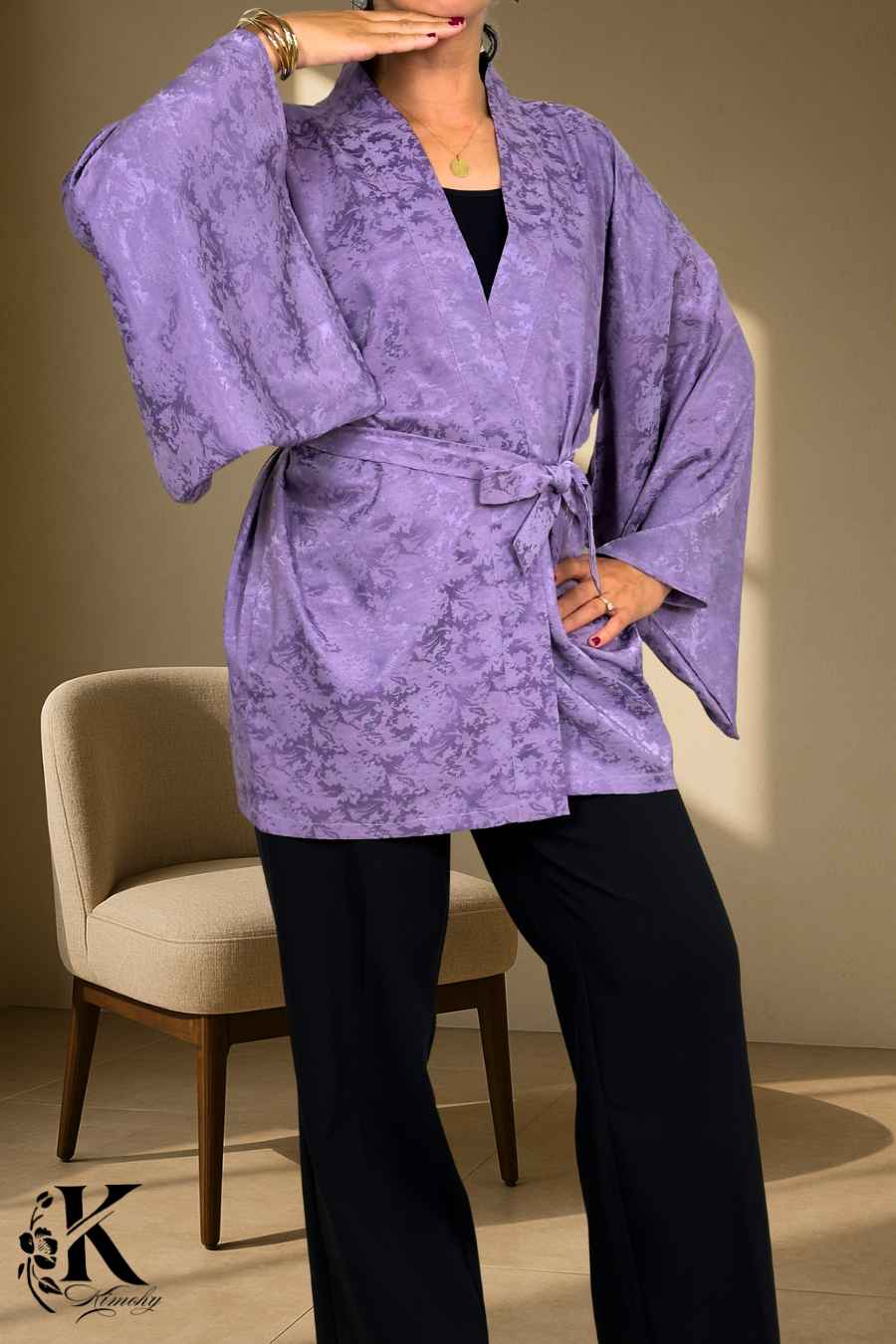 Veste kimono femme en tissu violet avec motifs subtils, portée avec un pantalon noir et un décor floral en arrière-plan
