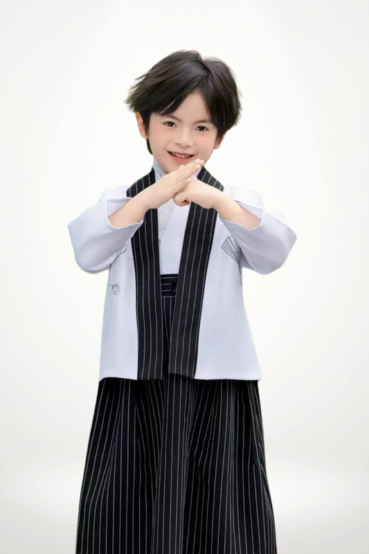 Un enfant porte un kimono blanc avec un pantalon noir à rayures, affichant une posture confiante et élégante