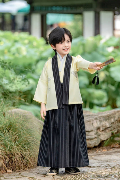 Un enfant porte un kimono traditionnel japonais blanc et noir, tenant un éventail jaune avec des motifs