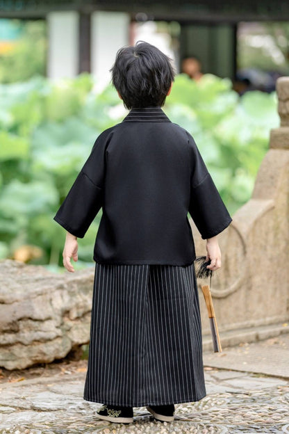 Enfant de dos portant un kimono noir avec des motifs en éventail, debout dans un jardin