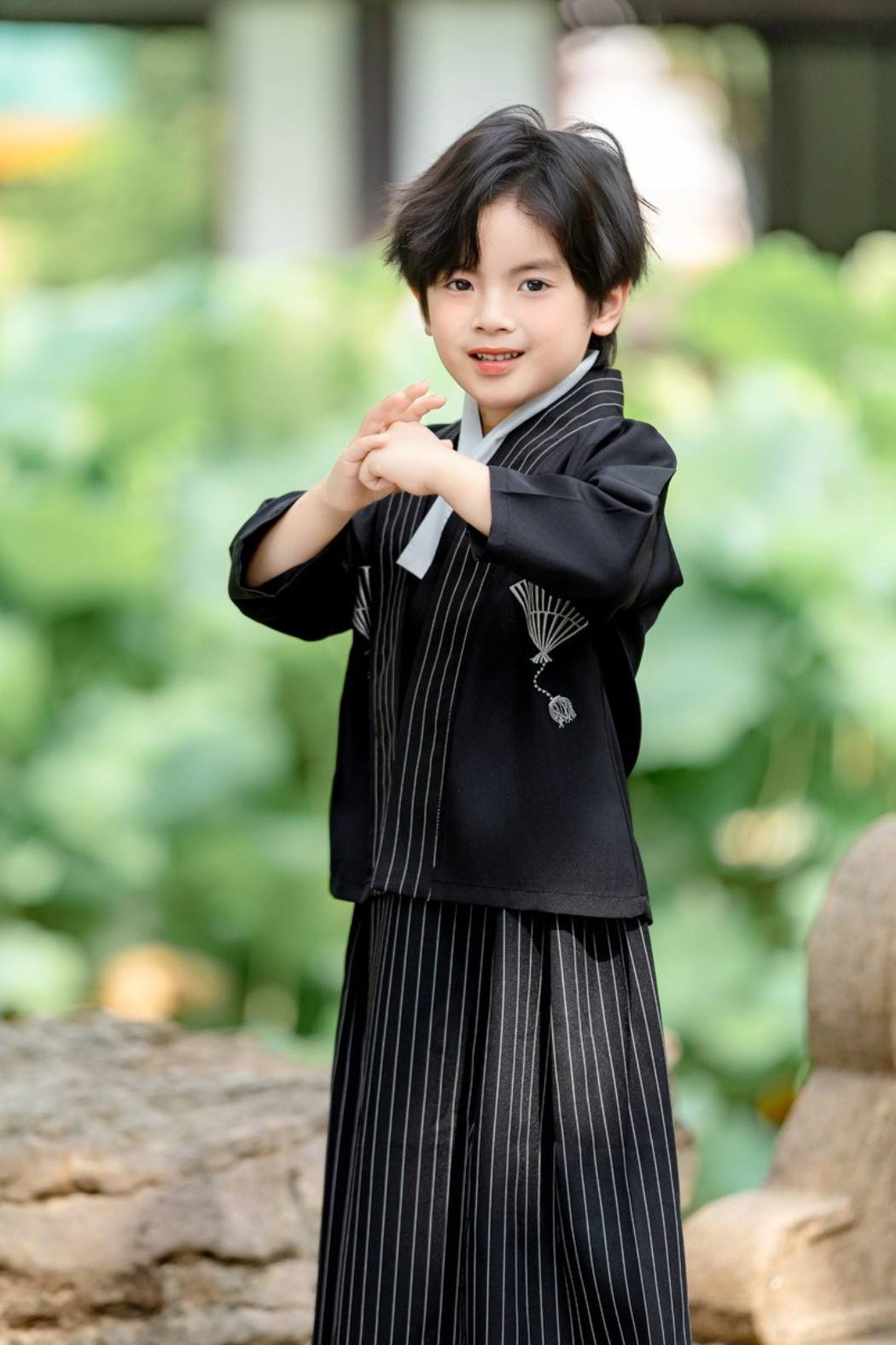 Enfant portant un kimono noir avec des motifs en éventail, debout dans un jardin