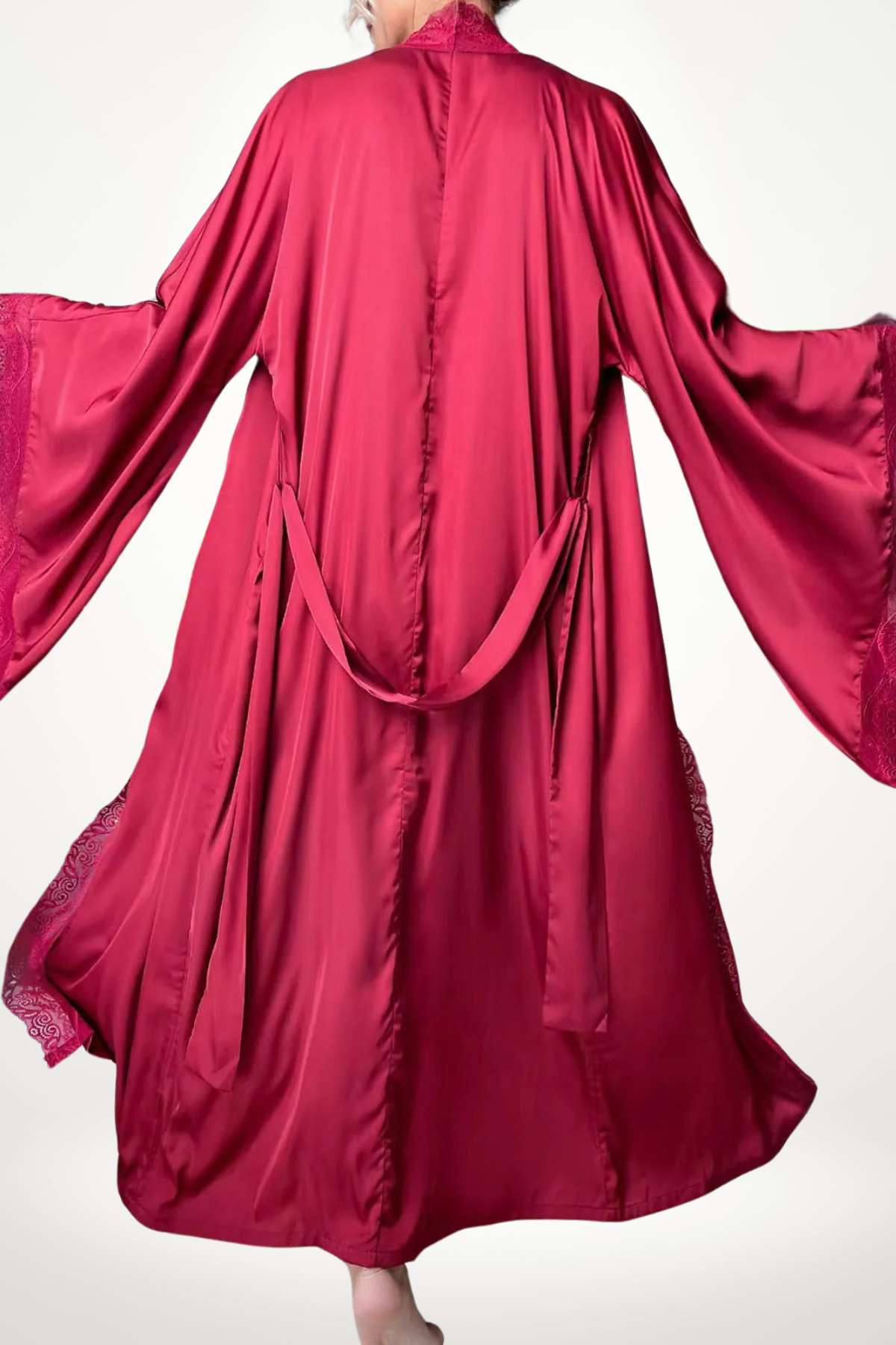Kimono rouge en satin avec des manches larges, décoré de dentelle, flottant élégamment dans un décor minimaliste