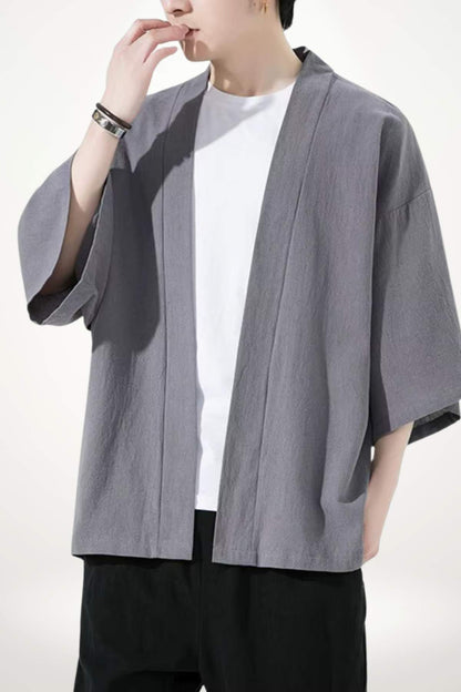 Homme portant un kimono gris moderne avec des manches larges, associé à un t-shirt blanc et un fond neutre