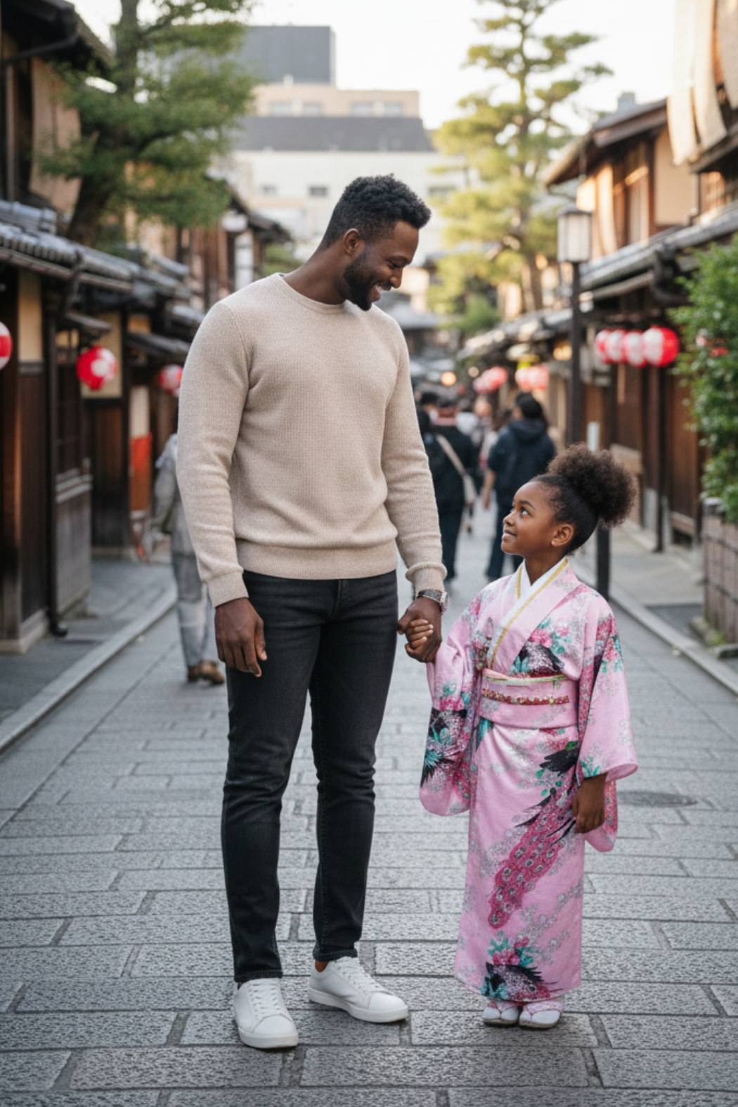 Une petite fille souriante porte un kimono rose orné de motifs floraux colorés et de manches larges dans une rue japonaise avec son papa