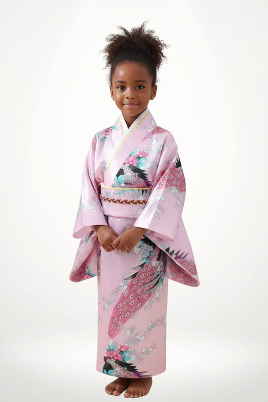 Une petite fille souriante porte un kimono rose orné de motifs floraux colorés et de manches larges