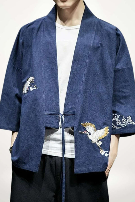 Kimono japonais homme indigo en coton tissé, veste sans boutons à œillets, coupe ample manches trois-quarts, broderie grue blanche et dorée.
