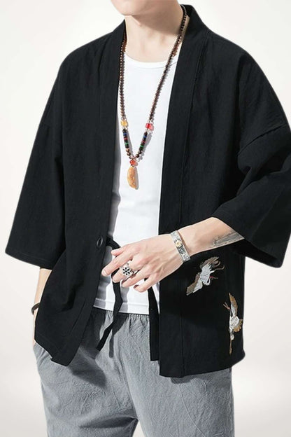 Homme portant un kimono noir avec des motifs de grues, associé à un t-shirt blanc et un pantalon gris