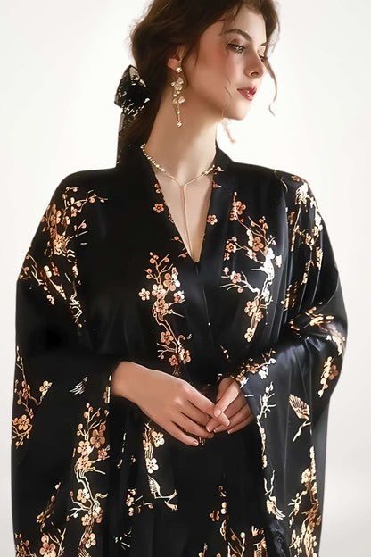 Femme portant un kimono noir en satin orné de motifs floraux dorés, posant élégamment avec des accessoires délicats