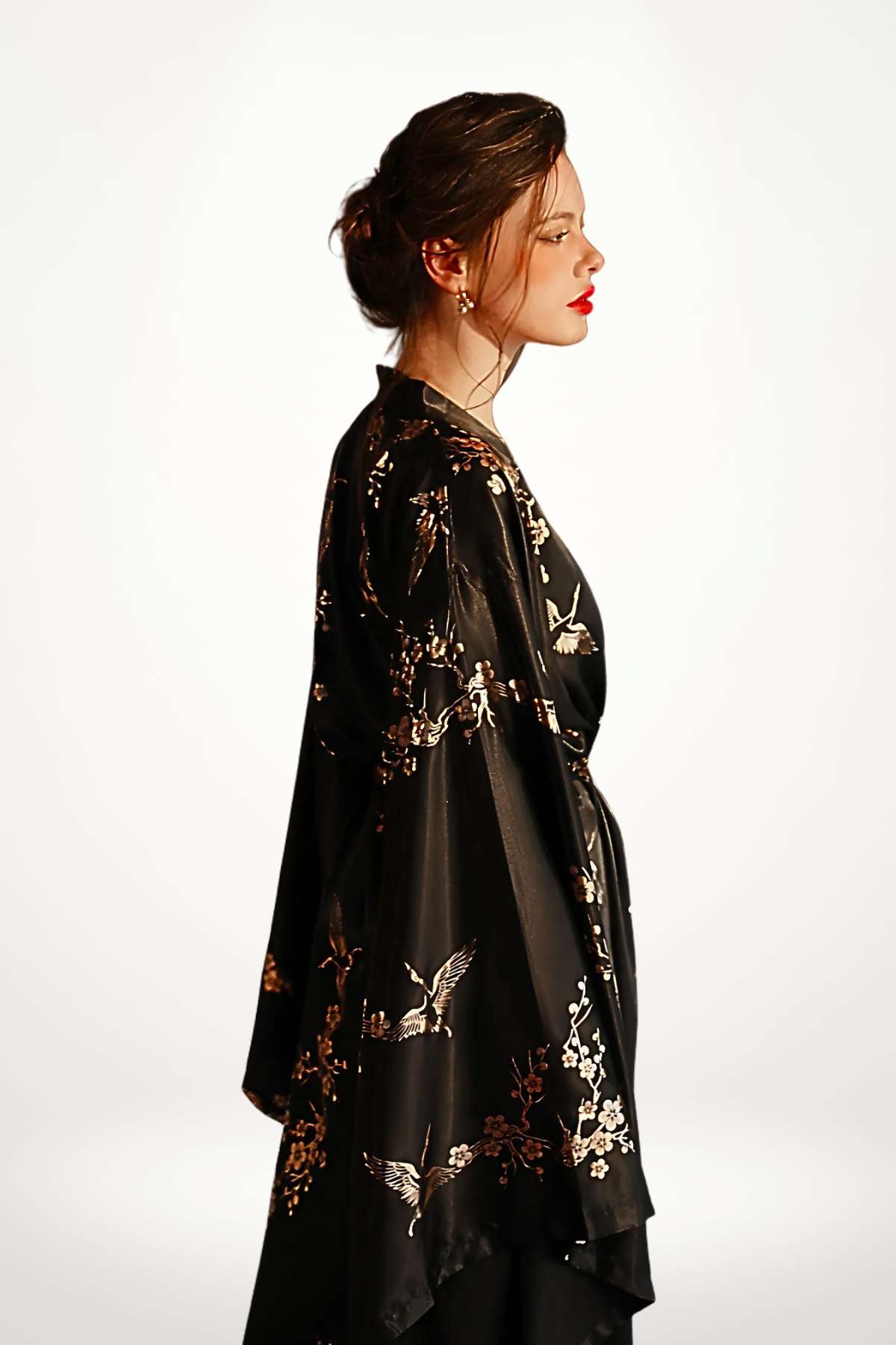 Femme en profil portant un kimono noir avec des motifs floraux dorés sur un fond blanc