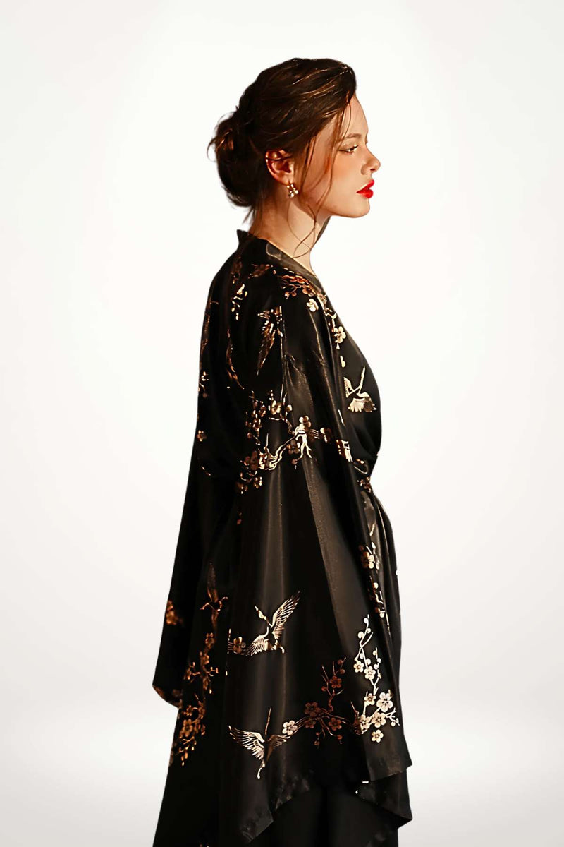 Femme en profil portant un kimono noir avec des motifs floraux dorés sur un fond blanc