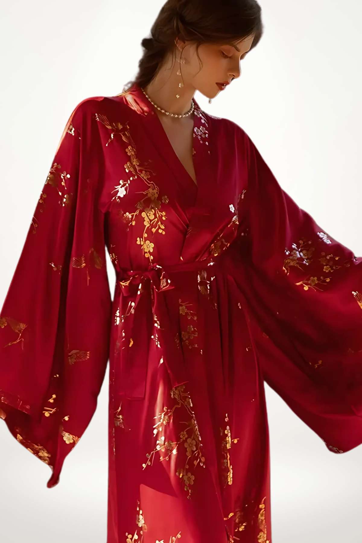 Kimono long en satin rouge, orné de motifs floraux dorés, porté avec élégance par une femme en posture gracieuse