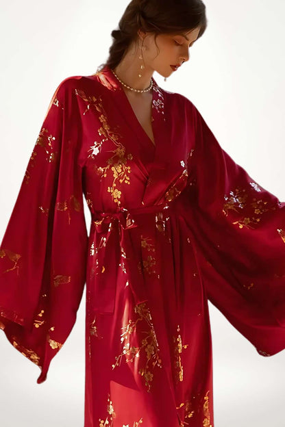 Kimono long en satin rouge, orné de motifs floraux dorés, porté avec élégance par une femme en posture gracieuse