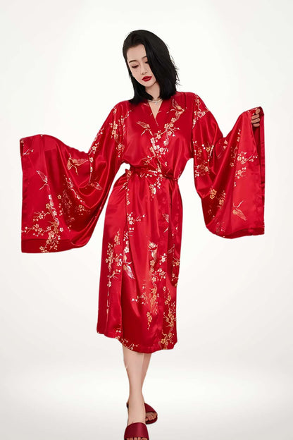 Femme en kimono long rouge brillant avec motifs floraux dorés, posant élégamment sur fond blanc