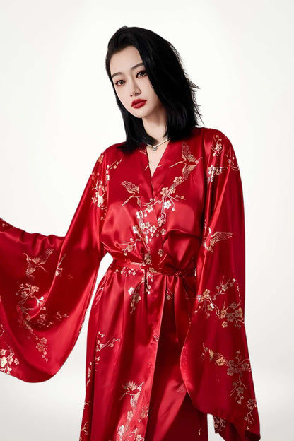 Femme portant un kimono long rouge en satin orné de motifs floraux et d'oiseaux, avec des manches larges