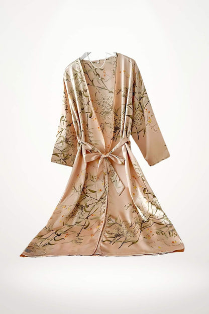 Peignoir kimono en satin rose avec motifs floraux verts et jaunes, noué à la taille, suspendu sur fond blanc