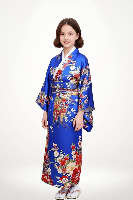 Fillette souriante en kimono bleu orné de fleurs colorées, posant avec grâce sur fond clair