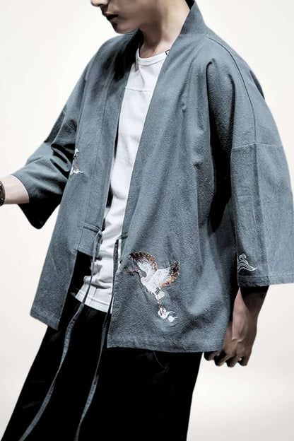 Homme portant un kimono gris avec des motifs d'oiseaux, dans une posture décontractée sur fond neutre