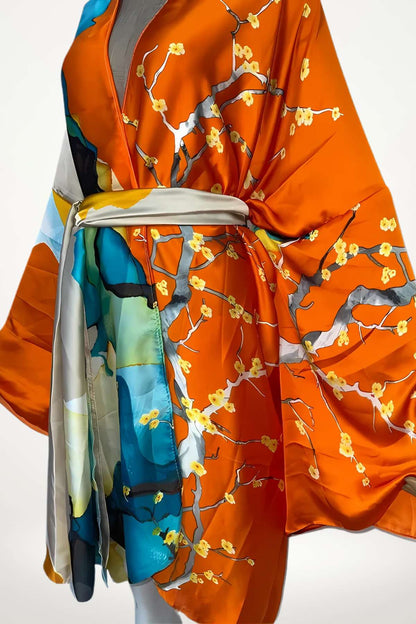 Kimono en satin orange avec motifs floraux jaunes et bleus, drapé élégamment, ceinture satinée grise