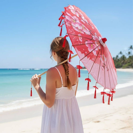 Femme portant une ombrelle rouge ornée de fleurs, se tenant sur une plage ensoleillée avec mer turquoise