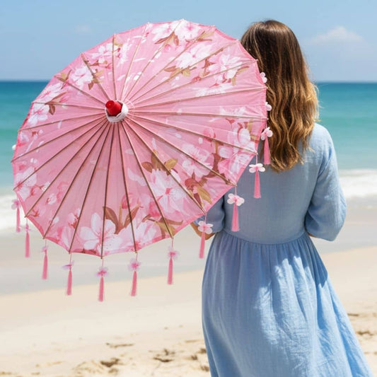 Femme de dos portant une robe bleue, tenant une ombrelle rose à fleurs sur une plage ensoleillée