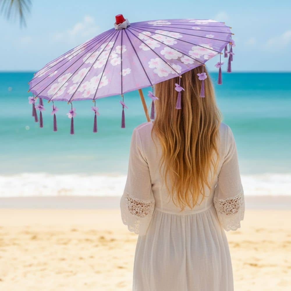 Femme aux longs cheveux blonds portant une ombrelle violette à motifs floraux sur une plage ensoleillée