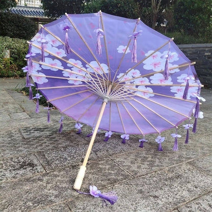 Ombrelle anti-UV adulte violette ornée de motifs nuageux et de franges, posée sur un sol en pierre