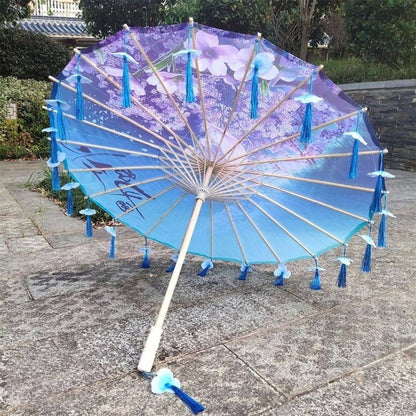 Ombrelle pliable bleu avec motifs floraux, décorée de pompons en tissu, posée sur un sol en pierre