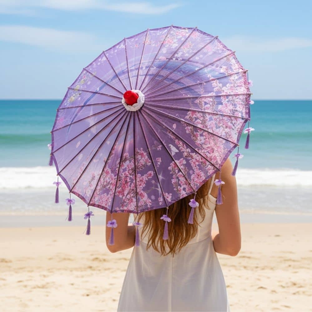 Ombrelle pliable violette avec motifs floraux, tenue par une femme face à la mer, ciel bleu en arrière-plan