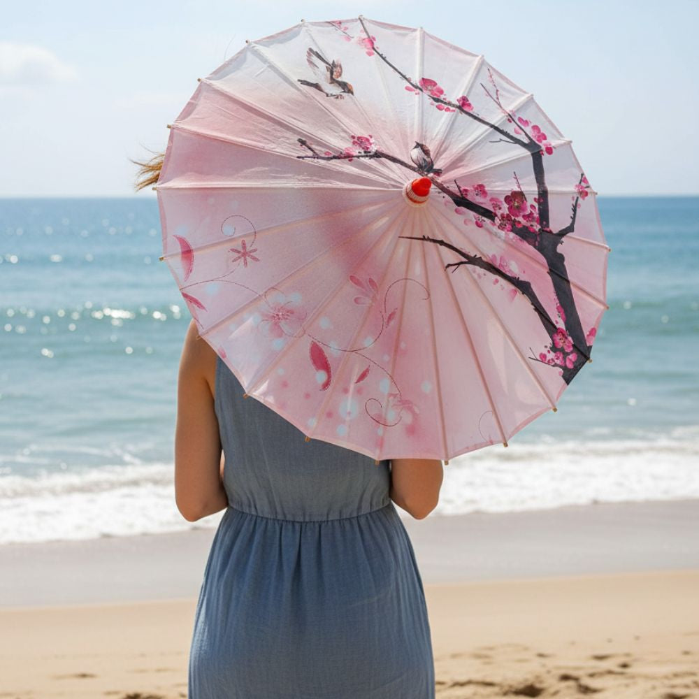 Ombrelle anti-UV rose ornée de fleurs et d'oiseaux, tenue par une femme sur la plage ensoleillée