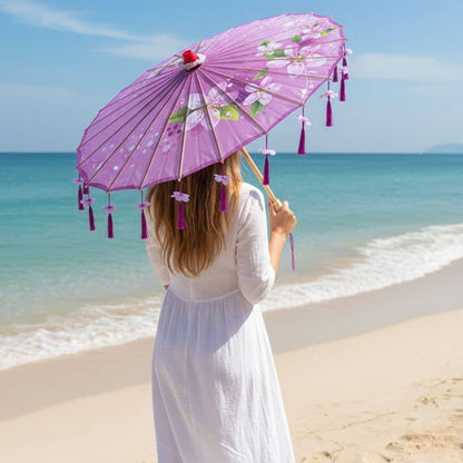 Femme de dos tenant une ombrelle violette décorée, sur une plage avec mer turquoise et ciel dégagé
