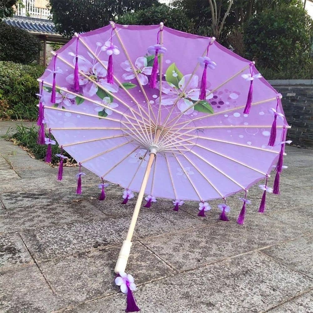 Ombrelle anti-UV pour adulte en violet avec motifs floraux et franges, posée sur un sol en pavés