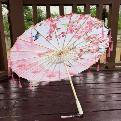 Ombrelle anti-UV pour femme, rose avec motifs floraux, décorée de franges, posée sur un sol en bois